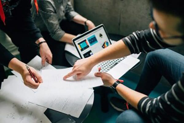 3 people in a meeting with one man pointing at a sheet of paper with graphs on it