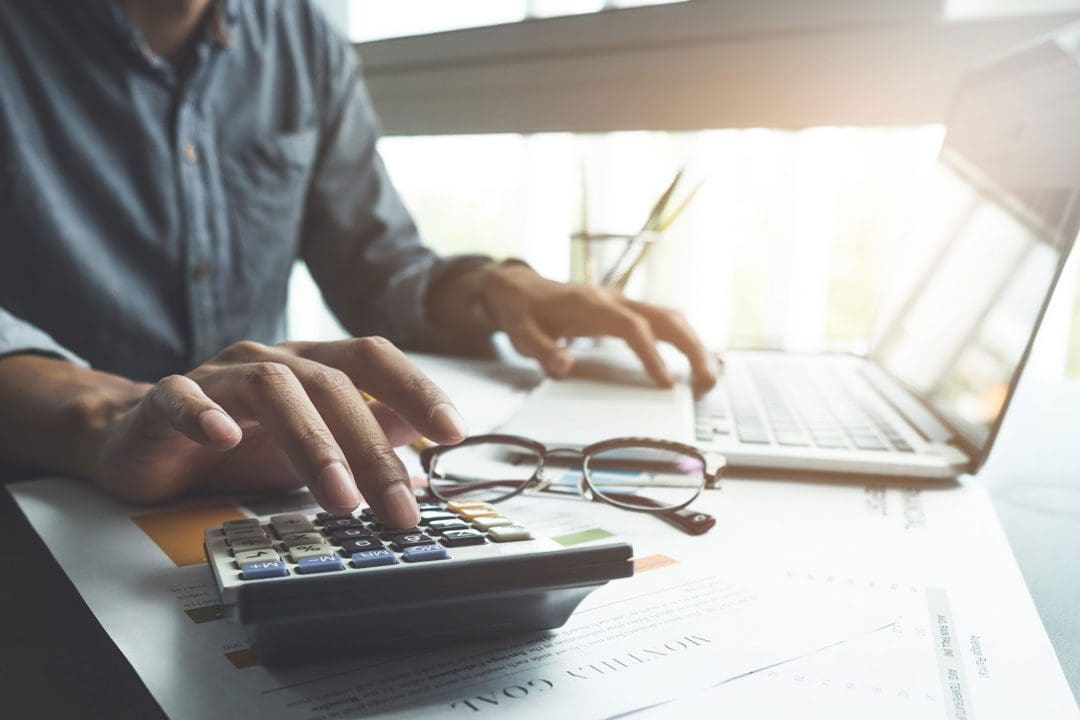close up, business man or lawyer accountant working on accounts using a calculator and laptop computer in his office