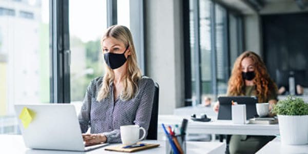 Woman wearing mask while sitting in office typing