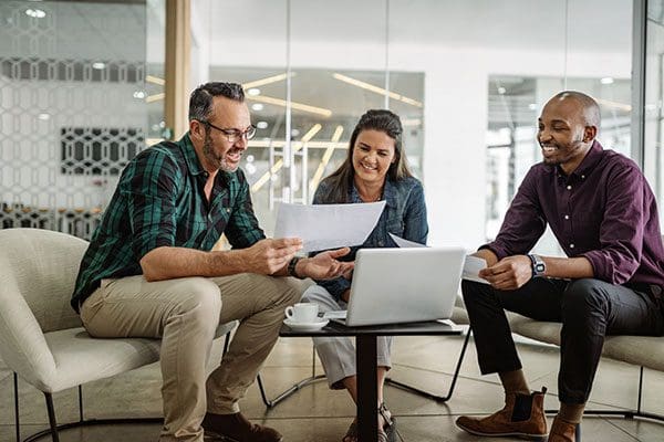 Three smiling diverse business colleagues having casual sit down business strategy meeting.