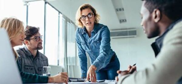 Meeting in office with woman speaking to a group of people and standing over them