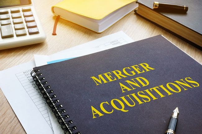Spiral notebook with Merger And Acquisition written in Large Text sitting on desk with papers, calculator, and two other books adjacent