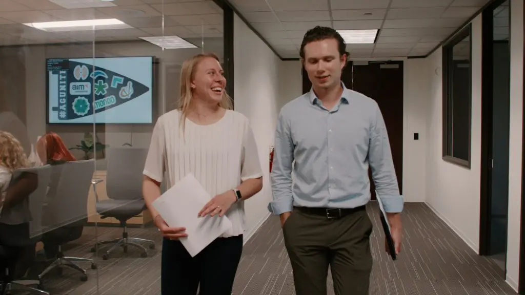 Women in white blouse walking with Man in blue dress shirt down team hallway