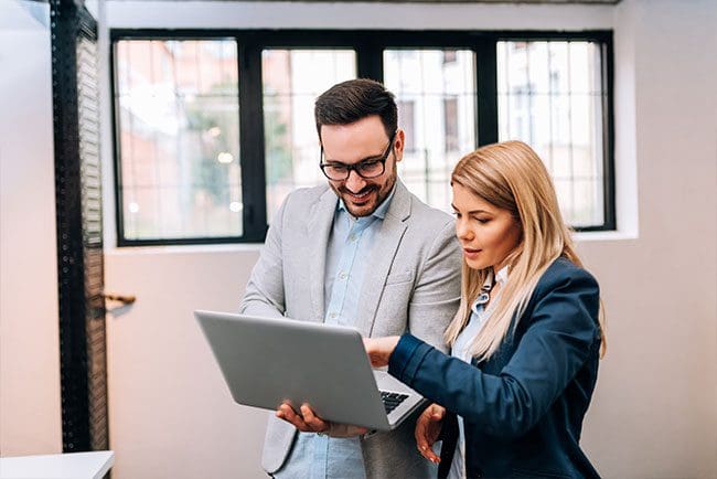 Young business man holding a laptop while discussing new project with his female colleague gue