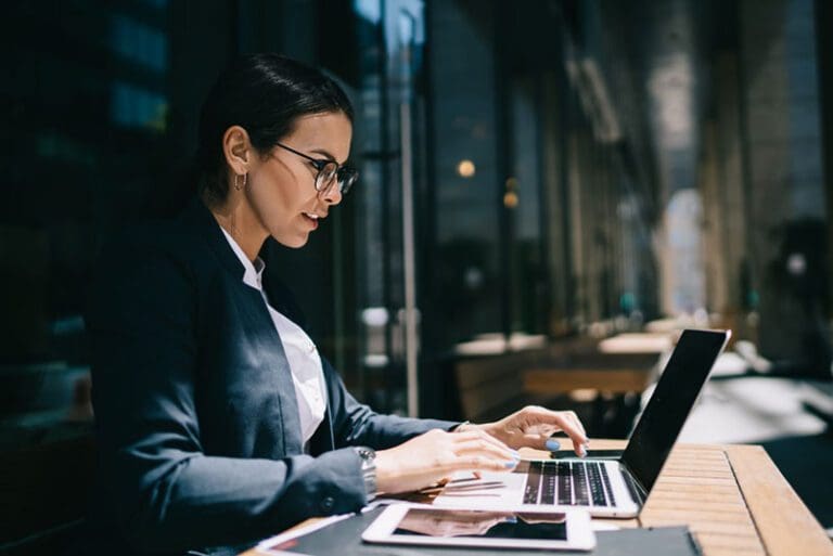 Side view of serious female economist working online with accounting documents on modern laptop device during sunny day in street cafeteria, caucasian ... See More